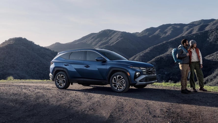 Two people standing next to a blue 2026 Hyundai Tucson SUV in the mountains