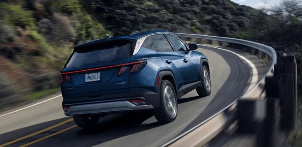 A blue 2026 Hyundai Tucson Hybrid SUV driving around the curve of a mountain road