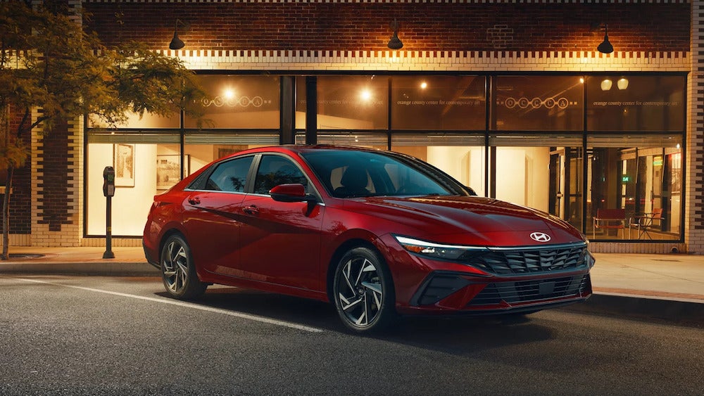 A red 2025 Hyundai Elantra parked in front of an illuminated store front at night