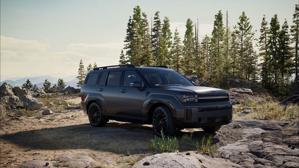 A black 2026 Hyundai Santa Fe SUV parked on the rocky top of a mountain, with pine trees in the background