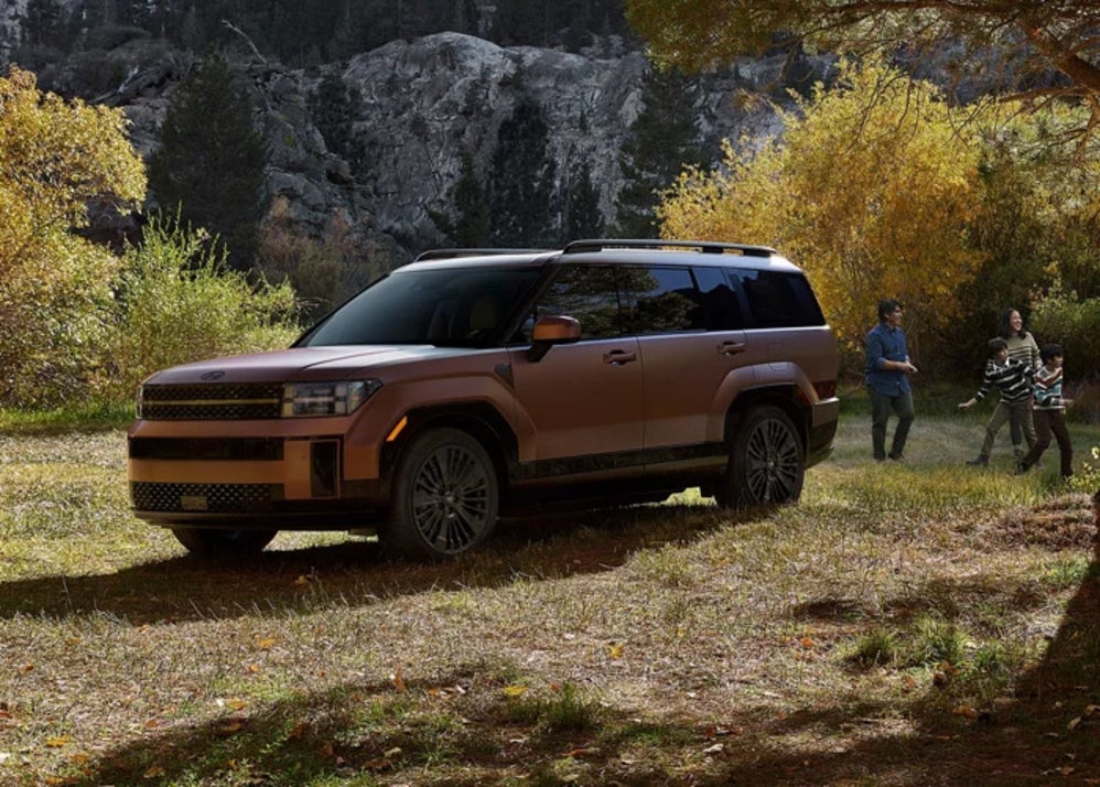 A copper 2026 Hyundai Santa Fe Hybrid SUV parked in a field with a family playing nearby