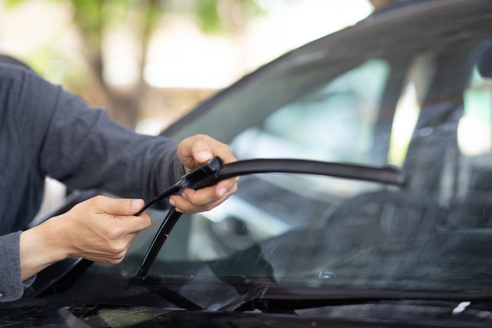 The arms of a white person in a gray shirt changing the windshield wiper blade of a vehicle