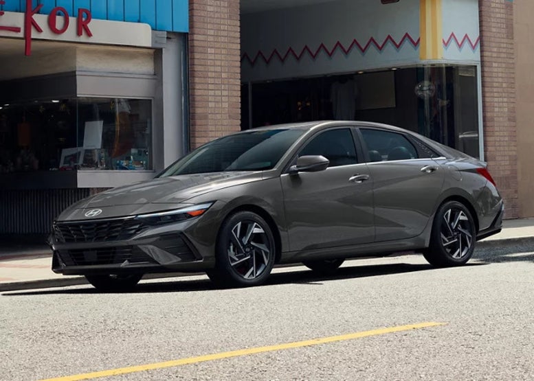 A gray 2025 Hyundai Elantra sedan parked in front of a storefront