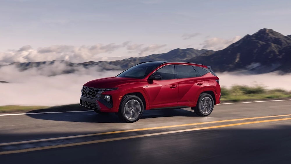 A red 2025 Hyundai Tucson Hybrid driving down a cloudy mountain road