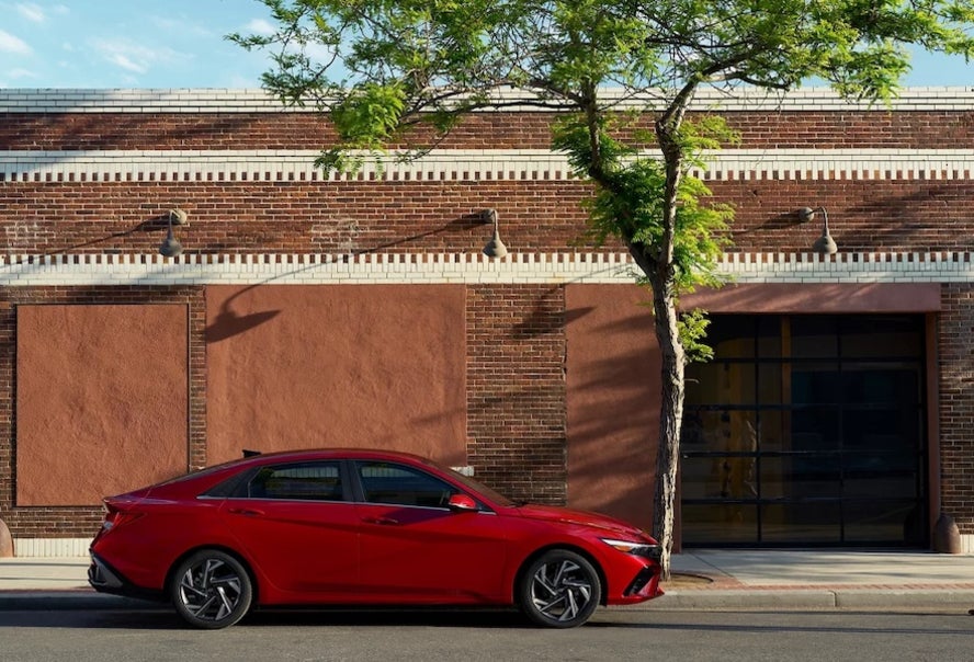 A red 2026 Hyundai Elantra sedan parked in front of a brick building