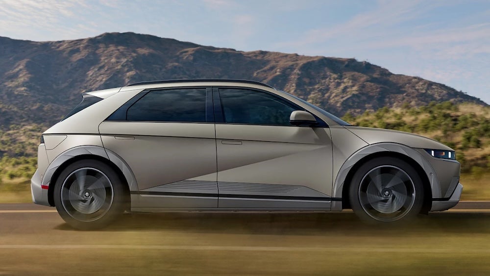 A side view of a gold 2026 Hyundai IONIQ 5 driving down a dirt road
