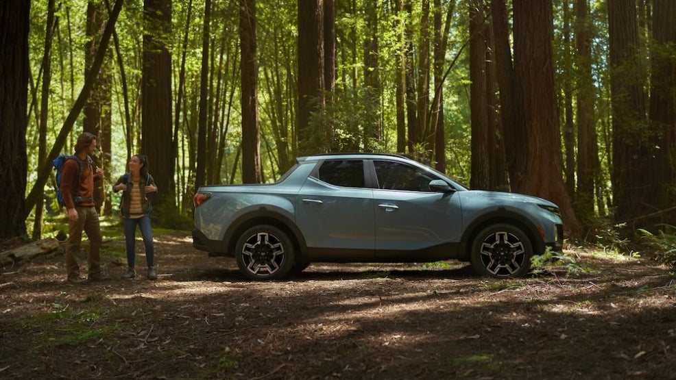 Two hikers standing beside a light blue 2026 Hyundai Santa Cruz