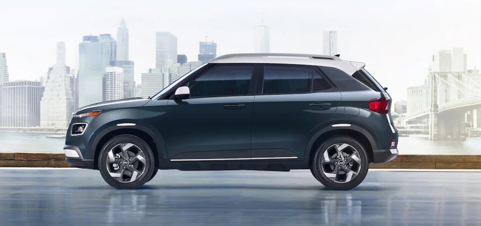 A side view of a slate gray 2026 Hyundai Venue SUV, with a city skyline in the distance