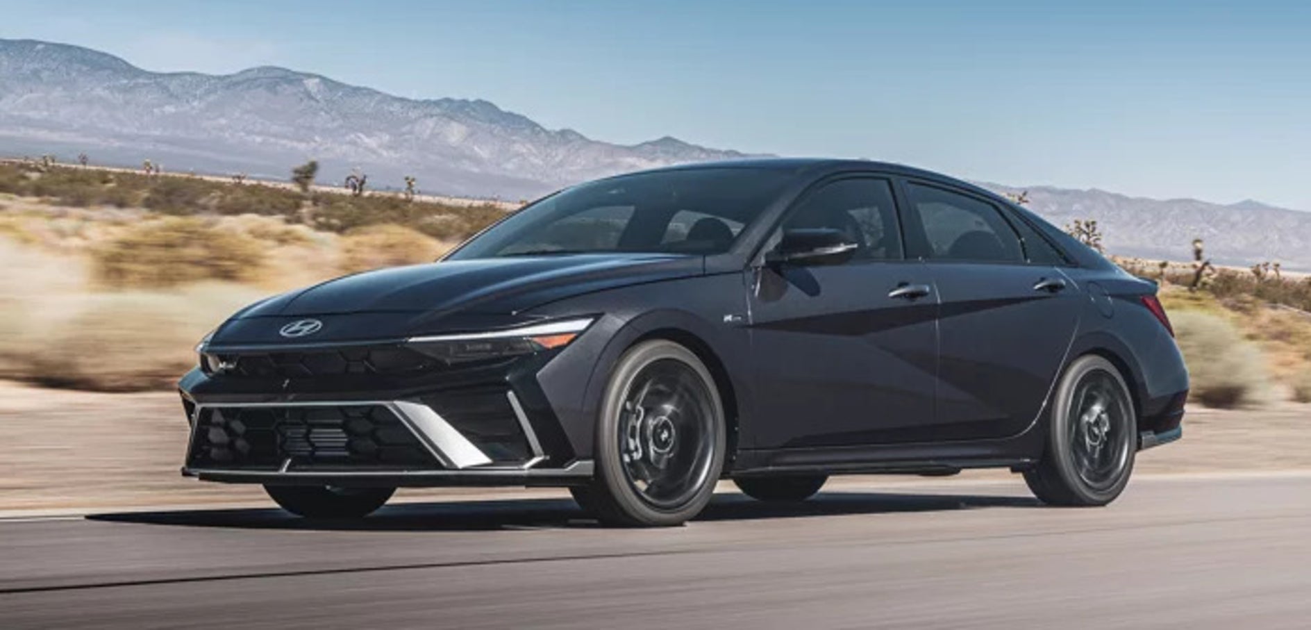 A dark gray 2025 Hyundai Elantra sedan driving through the desert, with mountains in the background
