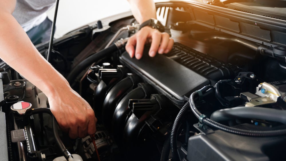 The arms of a person in a gray t-shirt working on the engine of a vehicle